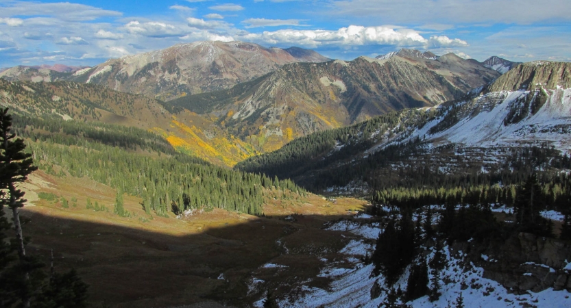 A vast mountainous landscape rests under a blue sky. There are snow in some parts of the scene. 